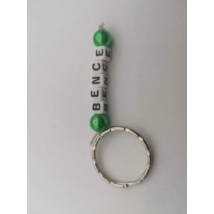 Ezüstszínű kulcskarikáról lelógó Bence szó betűgyöngyökből, két oldalán egy-egy gömbalakú, zöld gyönggyel. A betűgyöngyök kockaalakúak, fehér alapon feketék, elforgatva is ugyanazt mutatják.