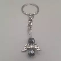 Ezüstszínű kulcskarikáról lelógó angyal kulcstartó: két fazettált gömbalakú ásványgyöngy között ezüstszínű, szívmintás szárny, tetején ezüst glória. Az ásványgyöngyök sötétezüst hematitok.