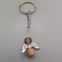 Ezüstszínű kulcskarikáról lelógó angyal kulcstartó: két gömbalakú gyöngy között ezüstszínű, szívmintás szárny, tetején ezüst glória. Az gyöngyök közül az alsó sárgás-narancssárgás, a teteje áttetsző barnás.