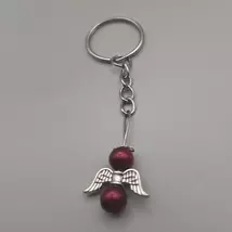 Ezüstszínű kulcskarikáról lelógó angyal kulcstartó: két gömbalakú gyöngy között ezüstszínű, szívmintás szárny, tetején ezüst glória. Az gyöngyök sötétpirosak.