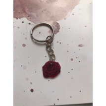 Ezüstszínű kulcskarikáról láncon lóg le egy piros rózsa.