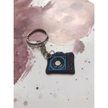 Ezüstszínű kulcskarikáról láncon lóg le egy fényképezőgép.