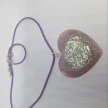 Lila zsinóros nyaklánc áttetsző, rózsaszínes, szív alakú műgyanta medállal, benne zöldes középrésszel és fehér, örvénylő mintával.