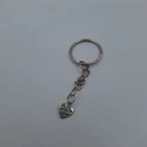 Ezüstszínű kulcstartó apró, szív alakú fém medállal, amelyen „Made with Love” felirat és egy kis szív motívum látható. A medál fém lánccal kapcsolódik a kulcskarikához.