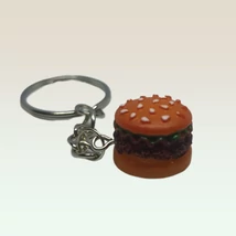 Ezüstszínű kulcskarikáról lánc lóg le, rajta medál: szezámmagos hamburger hússal, salátával, háromdimenziós.