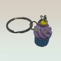 Ezüstszínű kulcskarikáról lánc lóg le, rajta medál: lila krémes muffin sárga szórócukrokkal.
