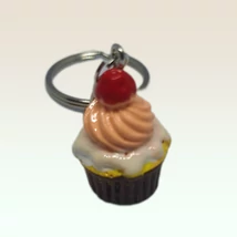 Ezüstszínű kulcskarikáról lánc lóg le, rajta medál: fehér mázas, papíros muffin, tetjén rózsaszín krémmel és egy cseresznyével.