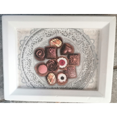 Fehér téglalapalakú gipsz képkeret közepén szalvéta kép: díszes tányéron különböző csokibonbonok, különleges mintájúak és alakúak. Köztük rózsás és szíves.
