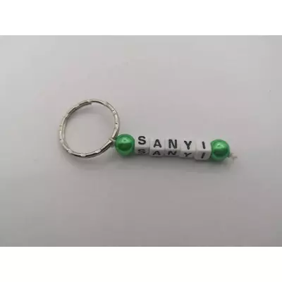 Ezüstszínű kulcskarikáról lelógó Sanyi szó betűgyöngyökből, két oldalán egy-egy gömbalakú, zöld gyönggyel. A betűgyöngyök kockaalakúak, fehér alapon feketék, elforgatva is ugyanazt mutatják. 