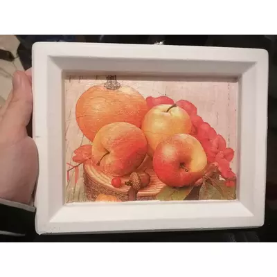 Fehér téglalapalakú gipsz képkeret közepén szalvéta kép: egy farönkön piros almák, virág, makk.