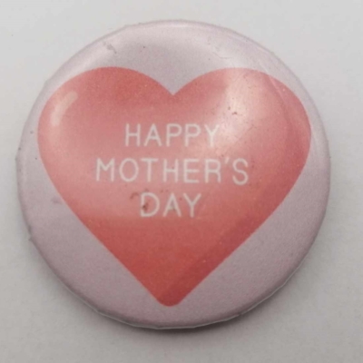 Köralakú kitűző rózsaszín alapon piros szívvel, rajta fehér felirat: Happy Mother's Day.