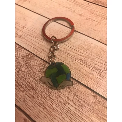 Ezüst kulcskarikán ezüst lánc lóg, föld bolygót ábrázolja amit két kéz tart, látszanak a tengerek és a fűves területek is. Köszönet::https://www.flaticon.com/authors/amonrat-rungreangfangsai