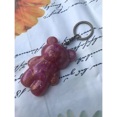 Ezüst kulcskarikán lánc, rajta szemes csavarral rögzített gyantakulcstartó. Rózsaszín mackó alakot fozmáz, végtagjai, feje, füle és orra tapintható. Helyenként aranyszínű. 