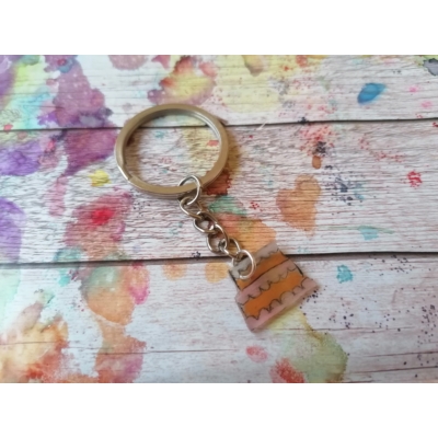 Ezüstszínű kulcskarikáról lelógó láncon kulcstartó: kétemeletes, narancssárga habos torta.