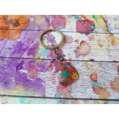 Ezüstszínű kulcskarikáról lelógó láncon kulcstartó: színes puzzledarabokból álló szív.