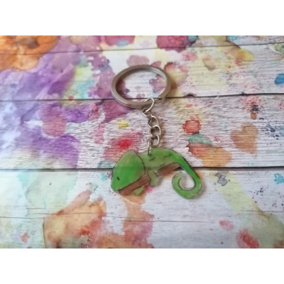 Ezüstszínű kulcskarikáról lelógó láncon kulcstartó: zöldszínű kaméleon fekszik egy faágon, farka kunkorodik.