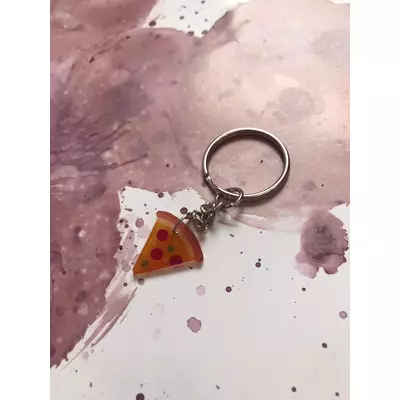 Ezüstszínű kulcskarikáról láncon lóg le egy darab pizza szelet szalámival.