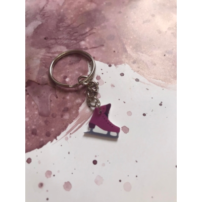 Ezüstszínű kulcskarikáról láncon lóg le egy lila színű jégkorcsolya.