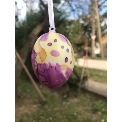 Sárga tojás lila mintával és pettyekkel, fehér szalagra fűzve.
