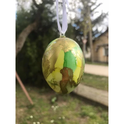 Márványmintás tojás fehér szalagra fűzve, sárga és zöld és arany színekben.