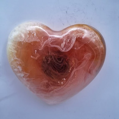 Szív alakú mágnes, amelyen halvány narancs és fehér színek keverednek, a középen található sötétebb tónusokkal. A színek elegáns spirál mintázatot alkotnak.