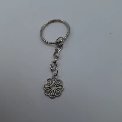 Ezüstszínű kulcskarikáról lánc lóg le, rajta ezüstszínű virág medál, domború szirmokkal.