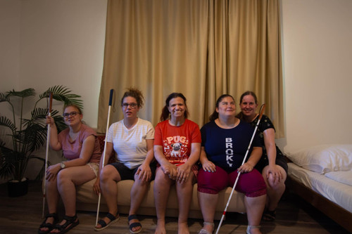 A képen egy szobában ülünk egymás mellett: Eszti, Dorina, Zsófi, Csilla, mellé guggolva Norina. Mindenki mosolyog. Esztinél, Dorinánál és Csillánál fehérbot.